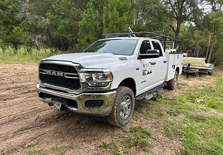 White RAM heavy-duty truck parked on a dirt path in a wooded area, towing a utility trailer.
