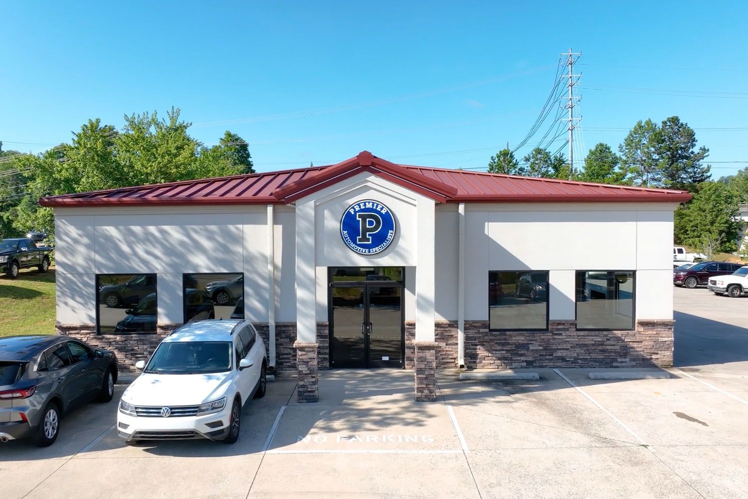 Exterior of a small white office building with a blue sign, red roof, and parked cars out front