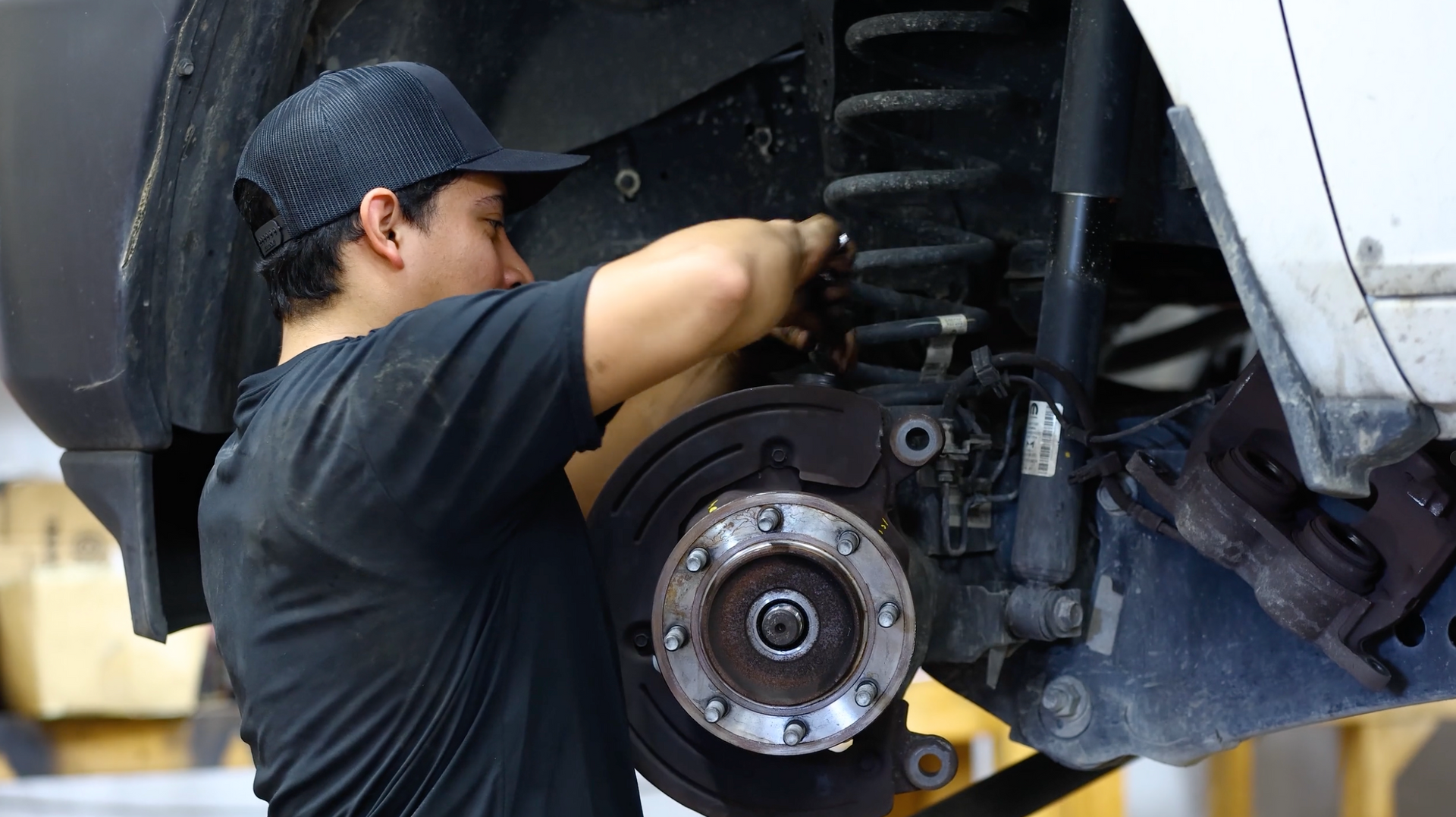 Mechanic working on a car’s exposed brake assembly inside a garage