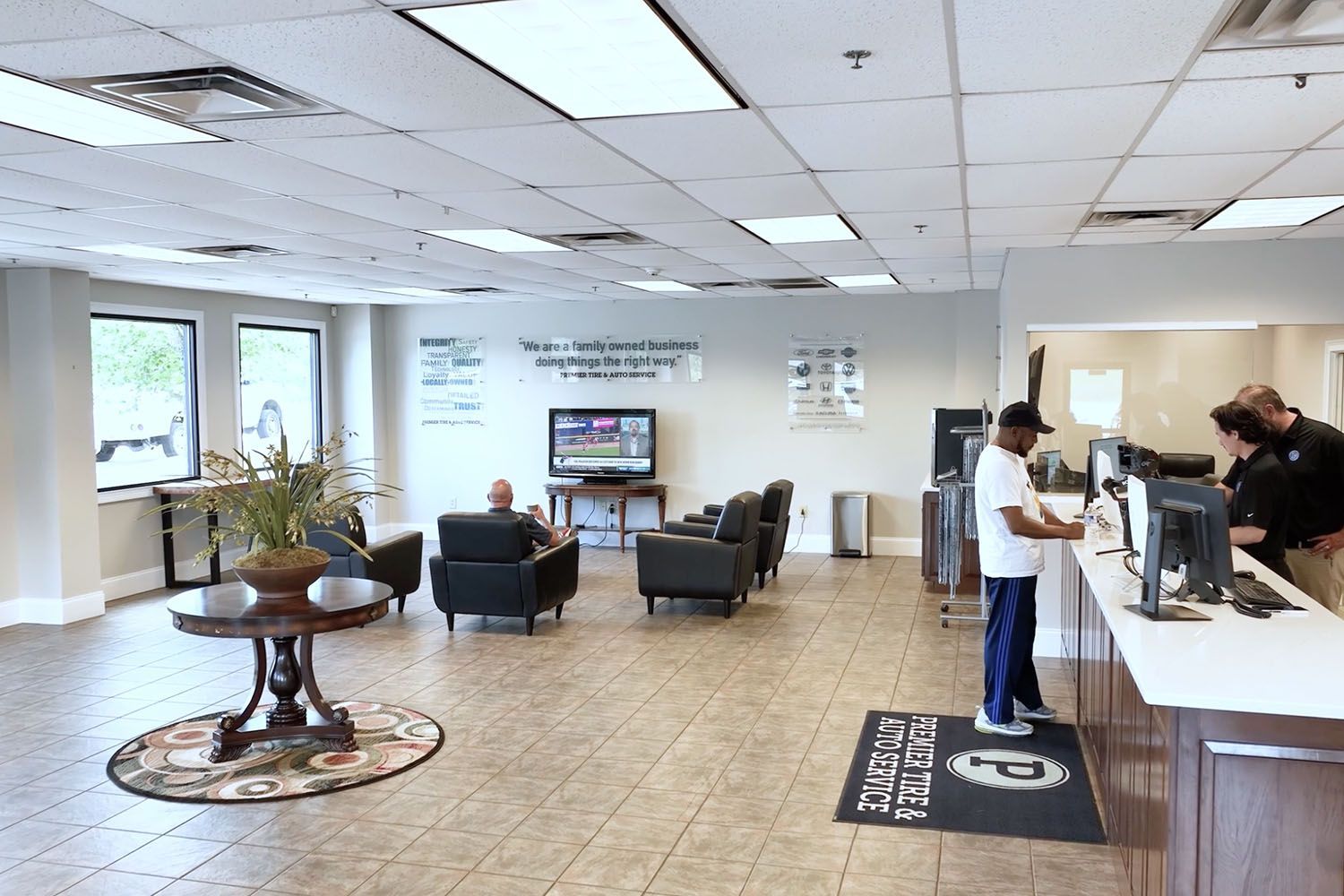 Bright lobby with seating area, reception counter, and people checking in near large windows.