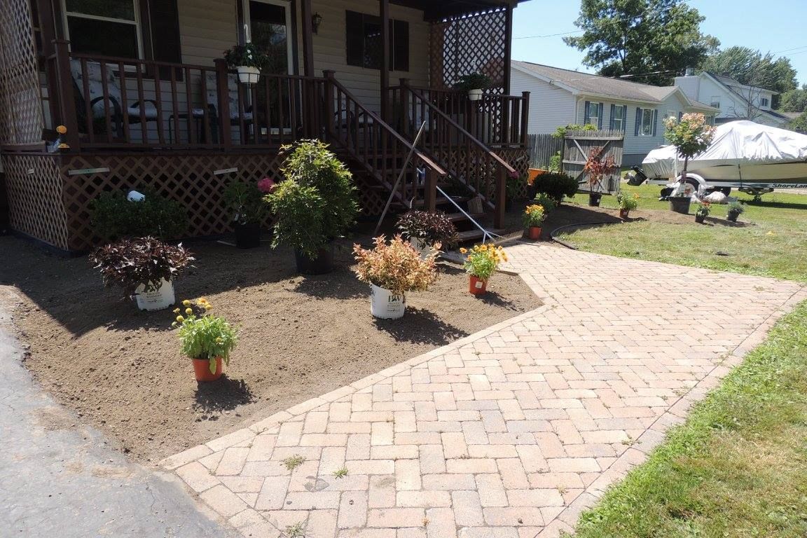 Front porch with potted plants and a brick walkway in a sunny yard