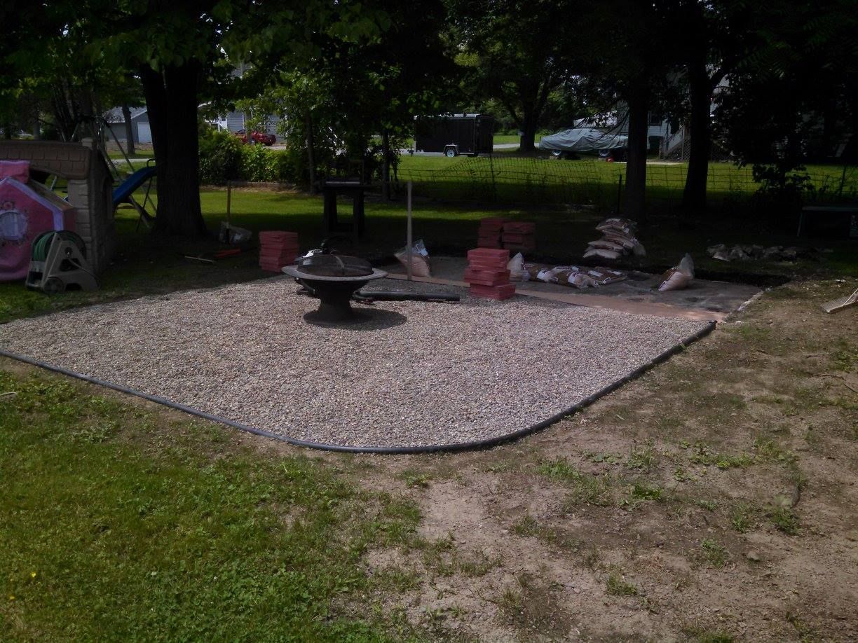 Gravel patio with a fire pit and red outdoor chairs under trees in a grassy yard