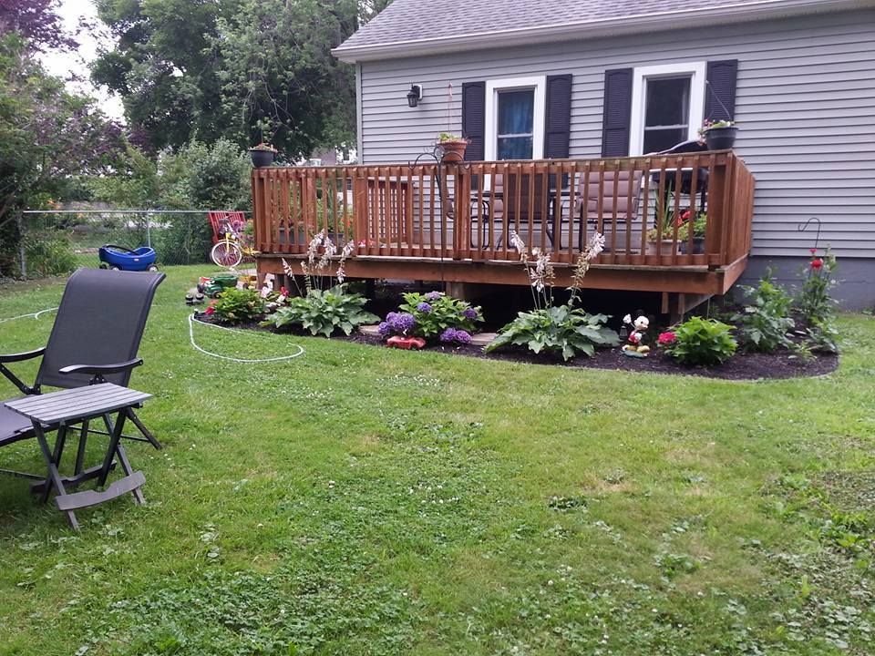 Backyard deck with potted flowers, lawn chairs, and a gray house in the background