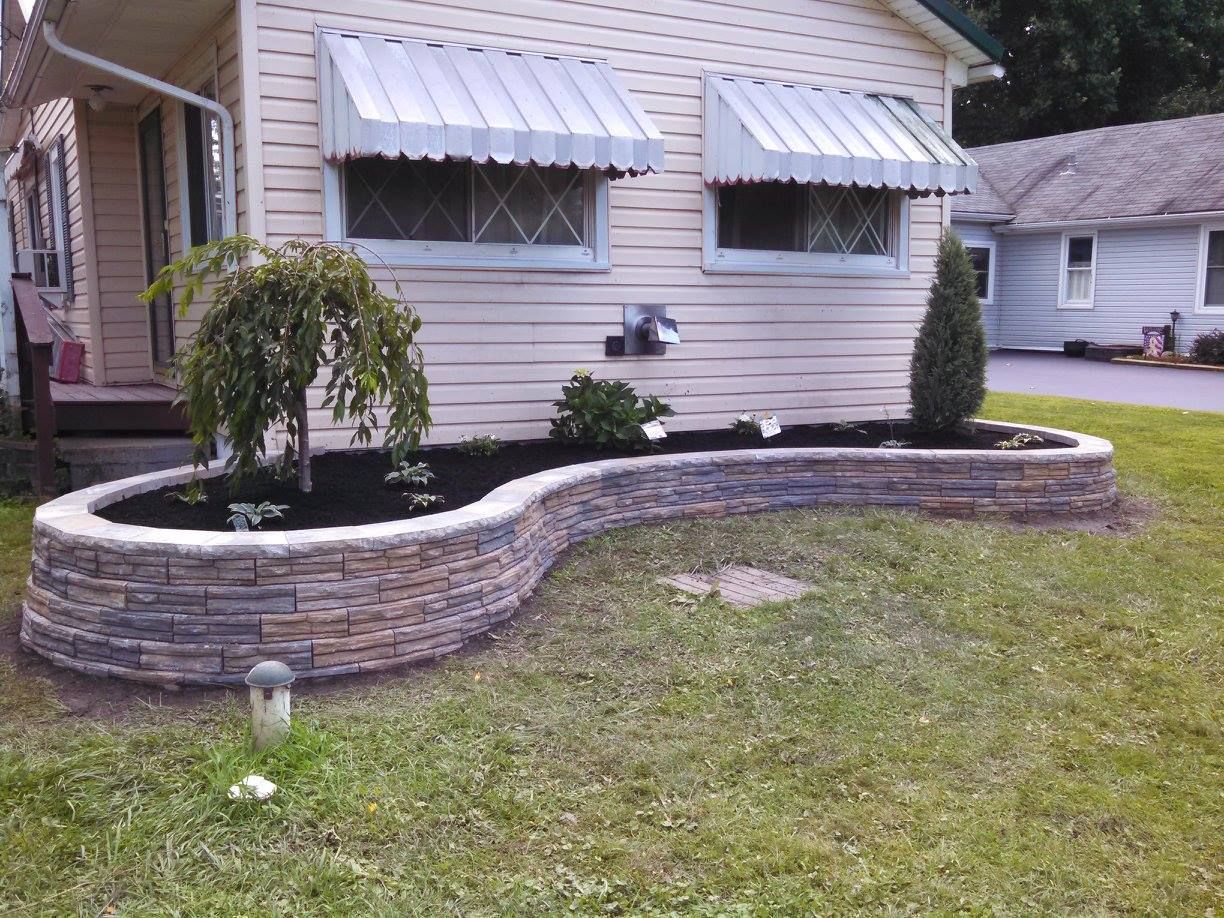 Front yard with curved stone planter, small tree, white house, and two windows with awnings