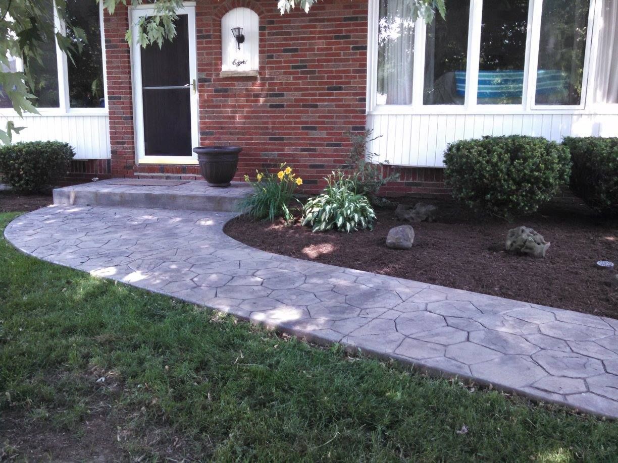 Front yard with curved stone walkway, brick house entrance, and landscaped shrubs and flowers