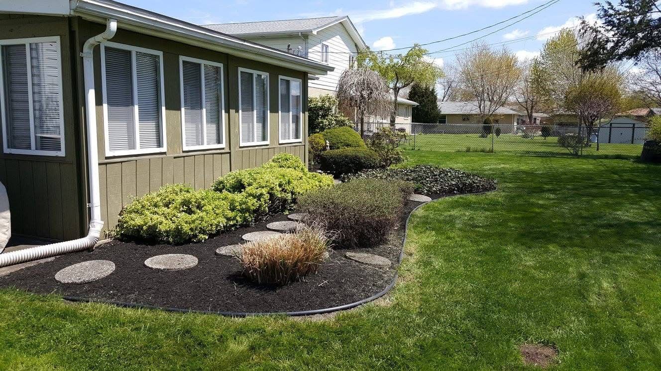 Small house exterior with a landscaped front yard, stepping stones, and green lawn under a sunny sky