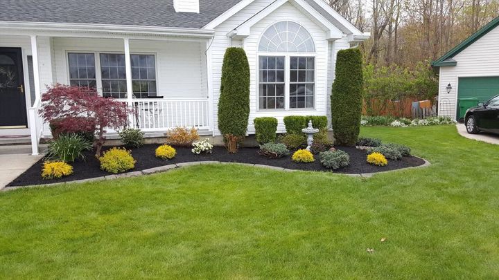 Front yard landscaping with a white house, green lawn, and yellow flowers around the walkway
