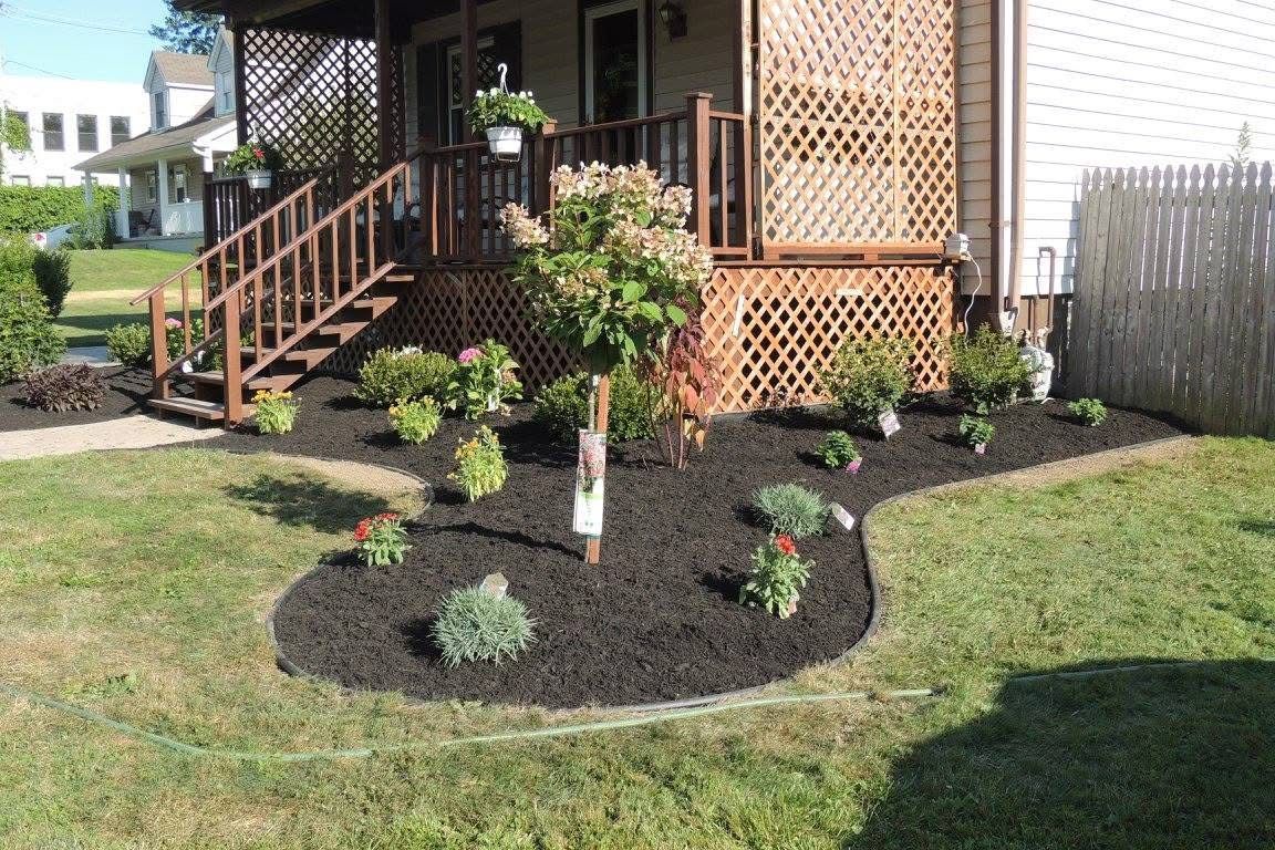 Landscaped front yard with dark mulch flower bed and small shrubs beside a porch and steps