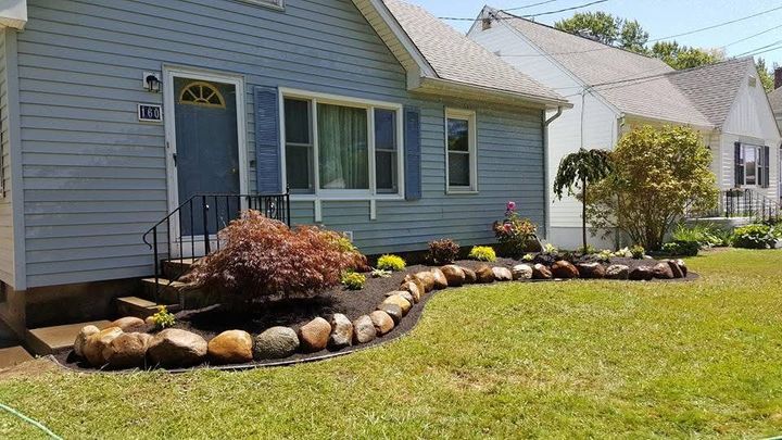 Blue house with white trim and a landscaped front yard bordered by rocks and shrubs.