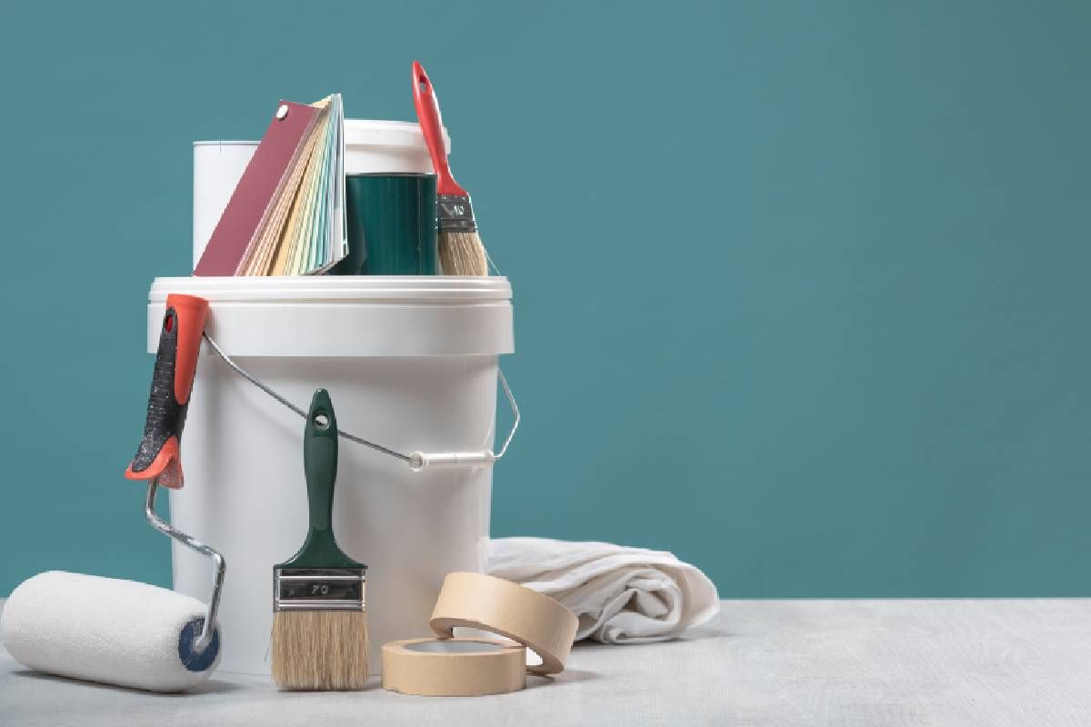 Bucket of paint with painting supplies stacked on top of it