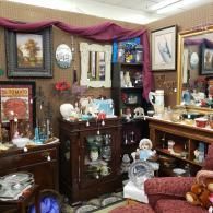 Cluttered antique shop display with wooden cabinets, framed art, mirrors, and assorted decorative items