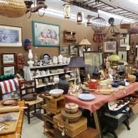 Antique shop interior crowded with vintage dishes, furniture, framed art, and lamps