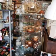 Glass display cabinet filled with assorted pottery and decorative bowls in a cluttered antique shop