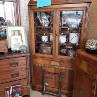 Wooden china cabinet with glass doors displaying white dishes in a room with matching furniture