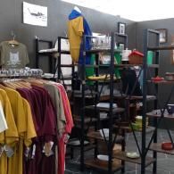 Clothing store interior with racks of shirts, shelves, and assorted shoes against gray walls
