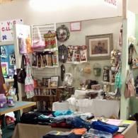 Cluttered gift shop display with hanging items, framed art, and colorful merchandise on tables