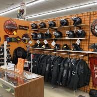 Motorcycle gear display with helmets, jackets, and accessories on shelves in a store.