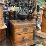 Vintage hand-crank coffee grinder on a wooden box, surrounded by antique items in a shop display.