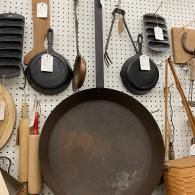 Kitchen wall with hanging cookware, wooden utensils, and a large black pan on a pegboard display