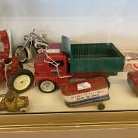 Red toy dump truck displayed on a shelf with other miniature vehicles.