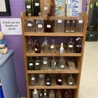 Wooden shelf of small bottles and jars in a store, with a sign promoting bath and body products.