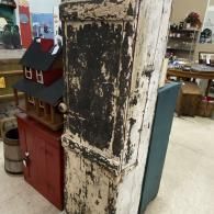 Distressed white wooden post beside a small red toy house in a shop interior