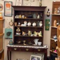 Antique wooden hutch displaying teapots, cups, and decorative ceramics in a shop or home setting