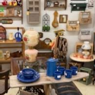 Eclectic shop display with blue dishes, lamps, and assorted vintage decor on shelves and tables