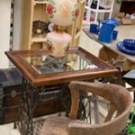 Antique wooden table with floral lamp, wicker chair, and blue dishes in a cluttered room