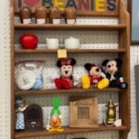 Shelf of assorted toys and decor, including Mickey Mouse figurines, a clock, a dollhouse, and a red vase.