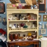 Cluttered shelf with assorted mugs, cups, and kitchenware in a cozy blue-walled room