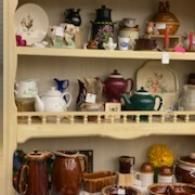 Shelves filled with assorted teapots and ceramic cups in a cozy display cabinet