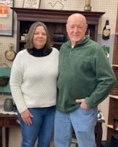 Two people standing together indoors in front of a fireplace, smiling at the camera.