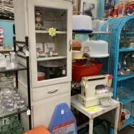 Store aisle with a white cabinet, blue shelves, and stacked household items and appliances.