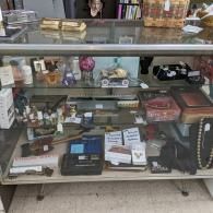 Glass display case filled with assorted small items, boxes, and jewelry in a store.