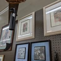 Framed artwork displayed on a pegboard wall in a shop or gallery interior.