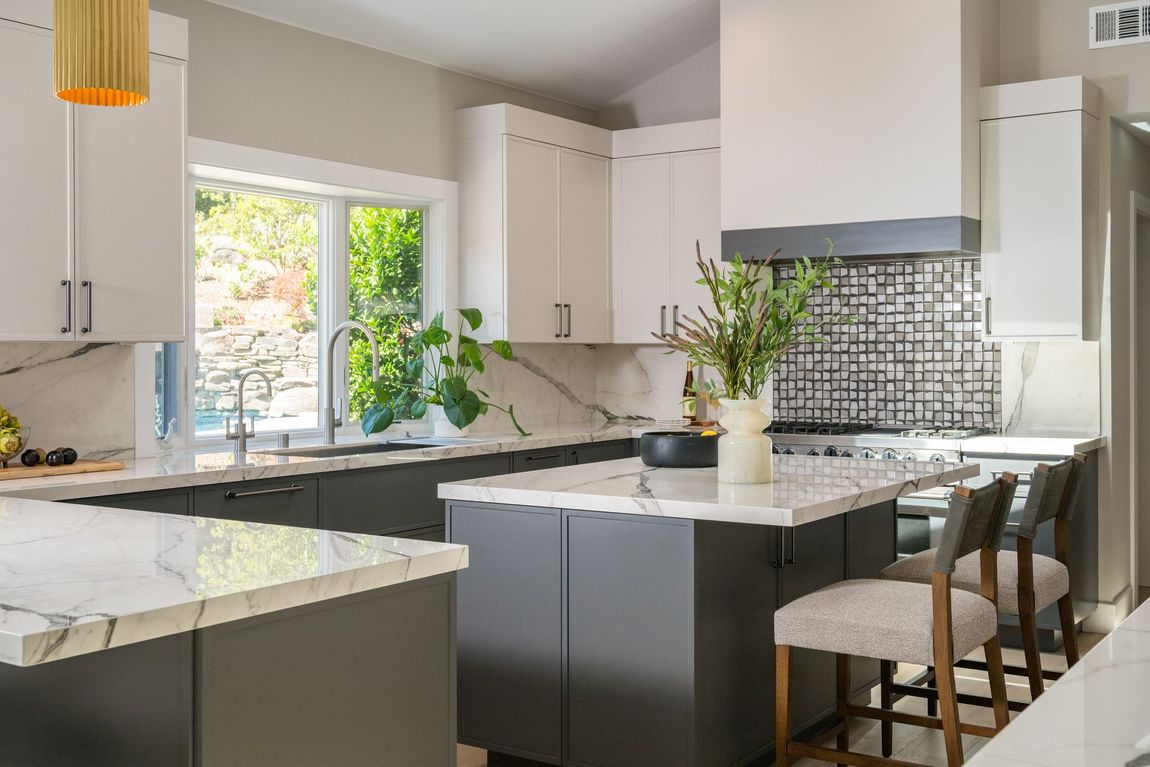 Modern kitchen with white and dark gray cabinets, white marble countertops, a central island, and two stools.