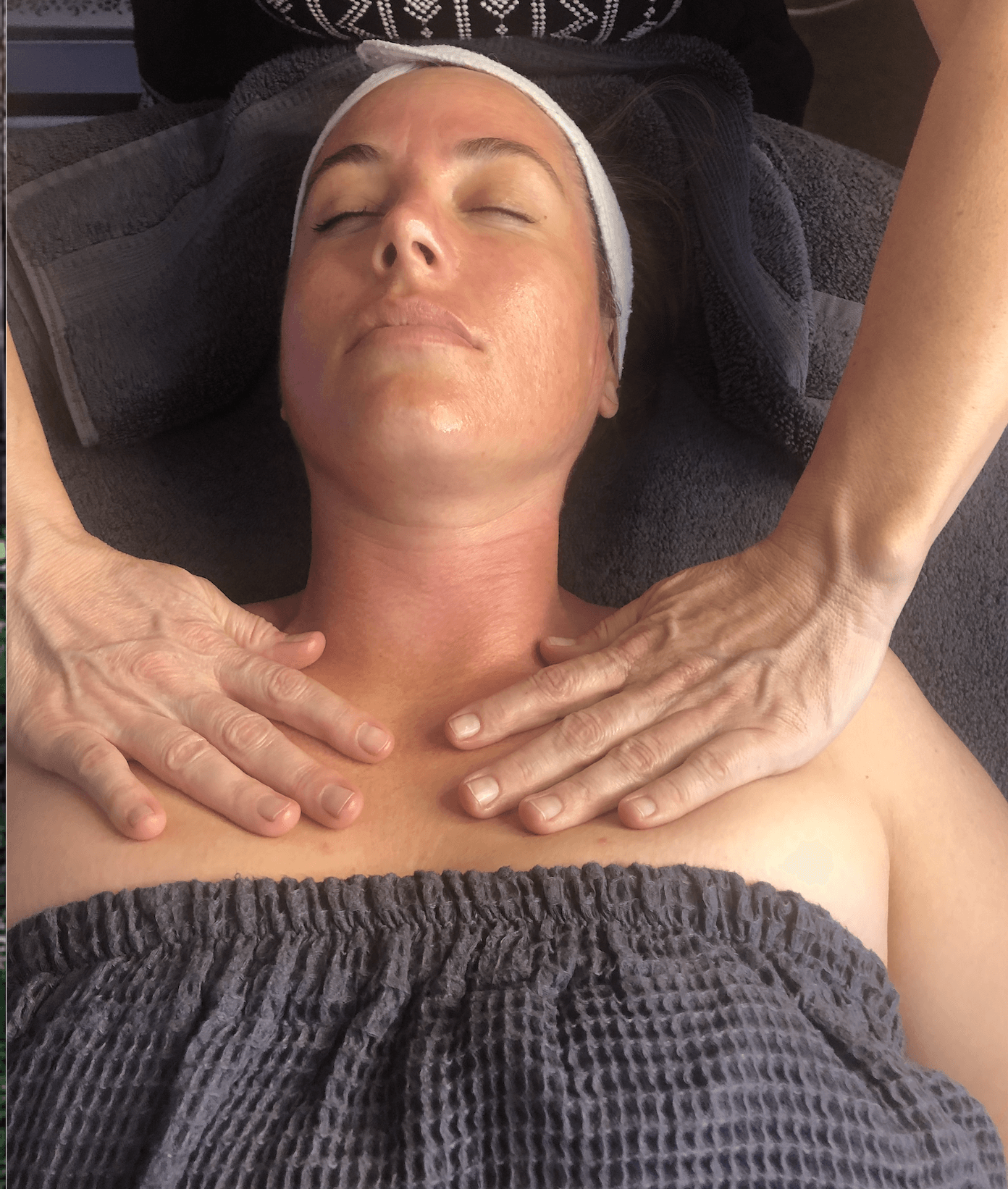 A professional massage therapist provides a chest and neck massage to a client lying down in a spa setting.