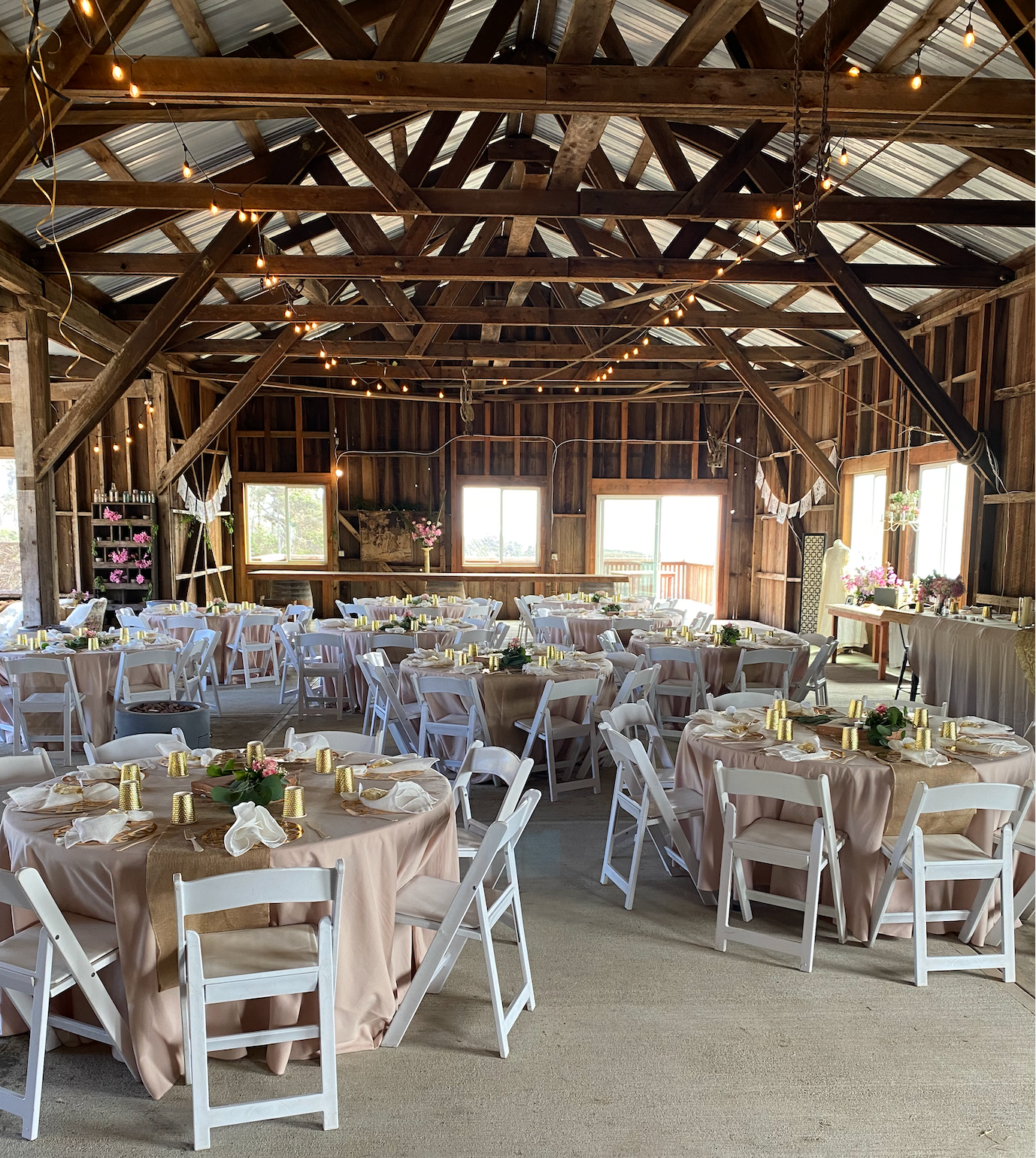 The Landing at Stewarts Point. Rustic barn interior set for a wedding reception with round tables, white chairs, and string lights across the ceiling.