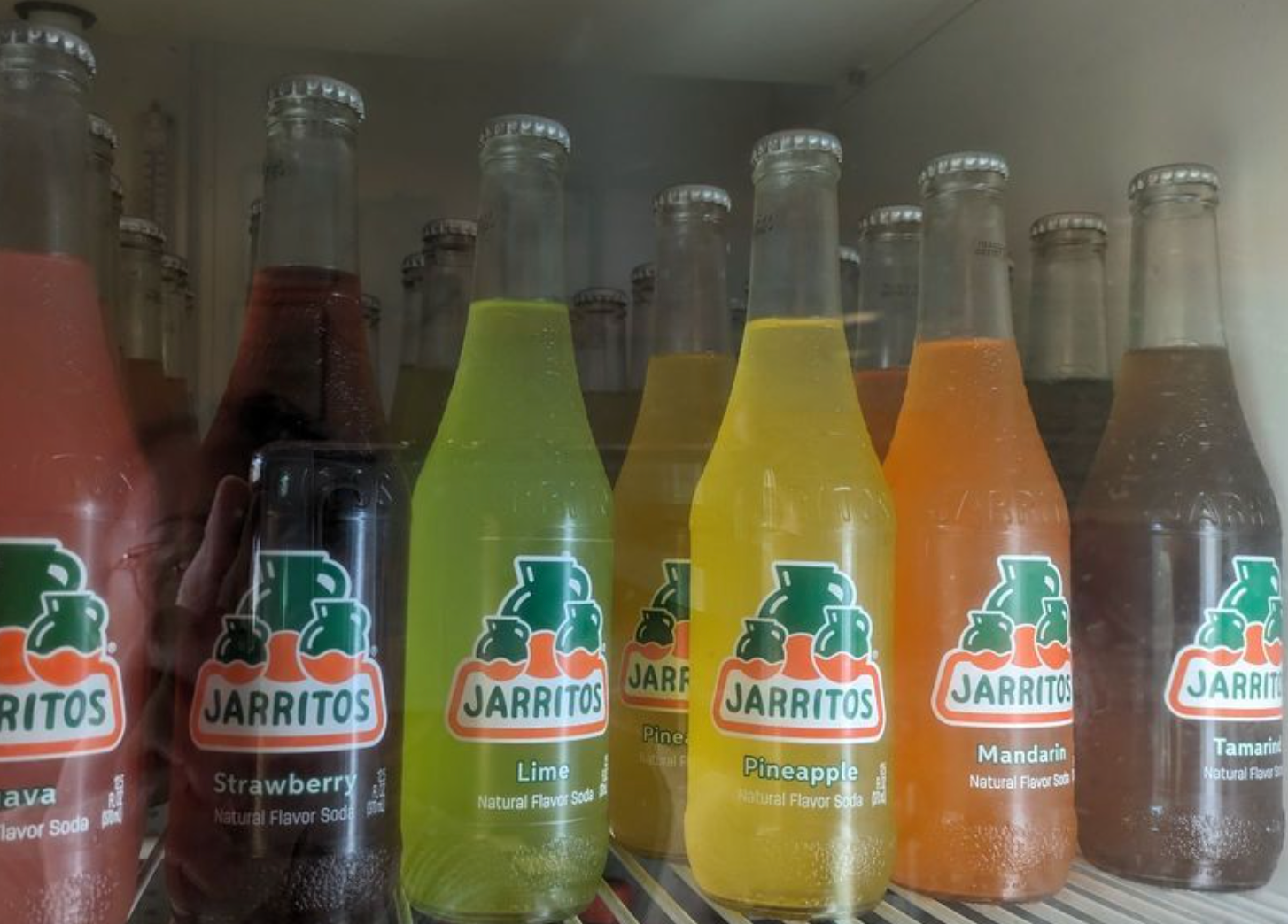 Multiple colorful glass bottles of Jarritos soda displayed on shelves in a refrigerator.
