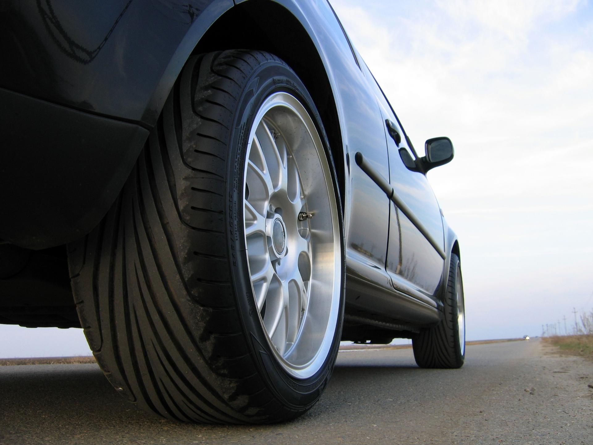 Low-angle view of a black car’s front tire and wheel on a road
