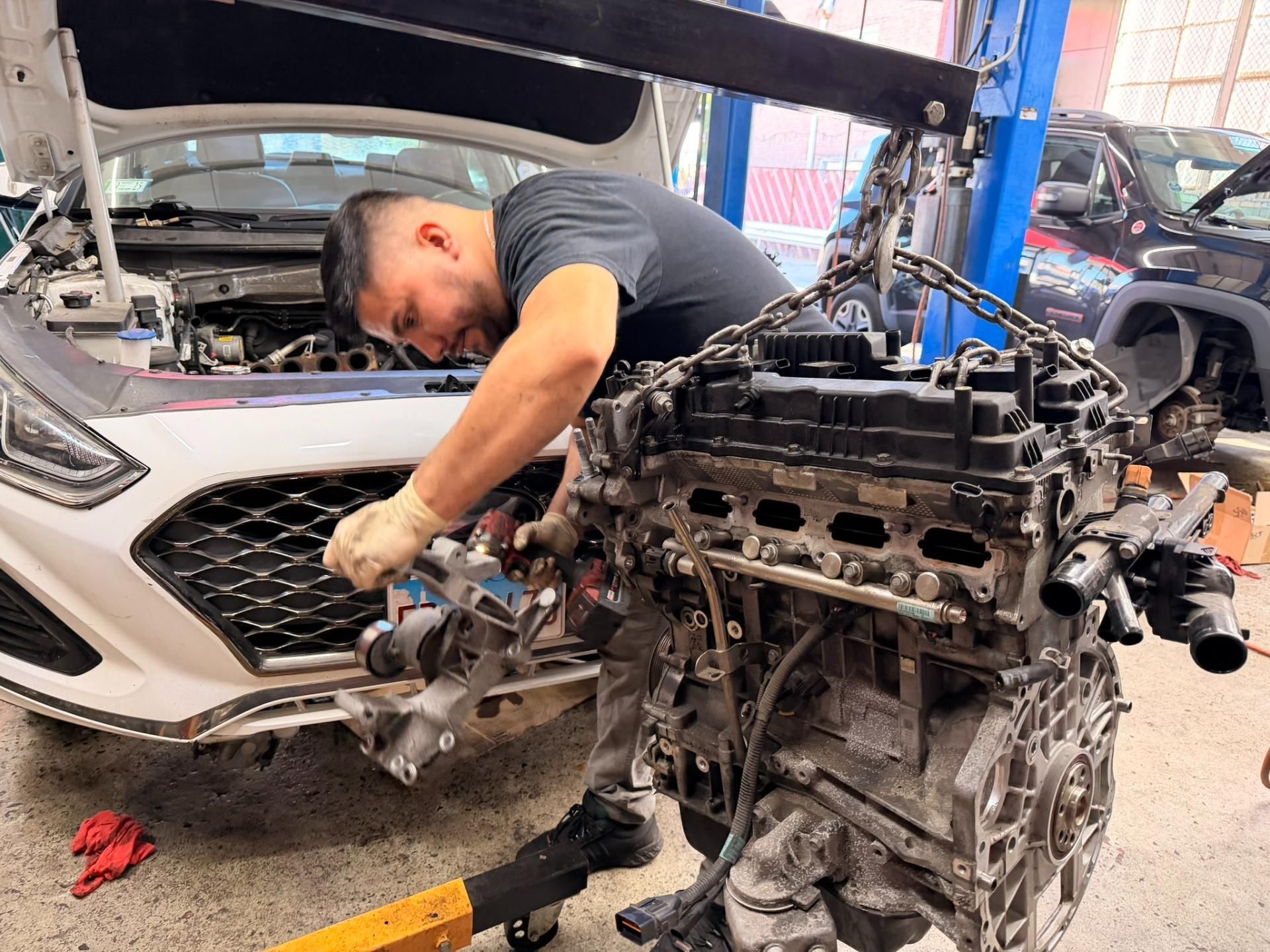 Mechanic working on a car engine in a repair shop with the hood open