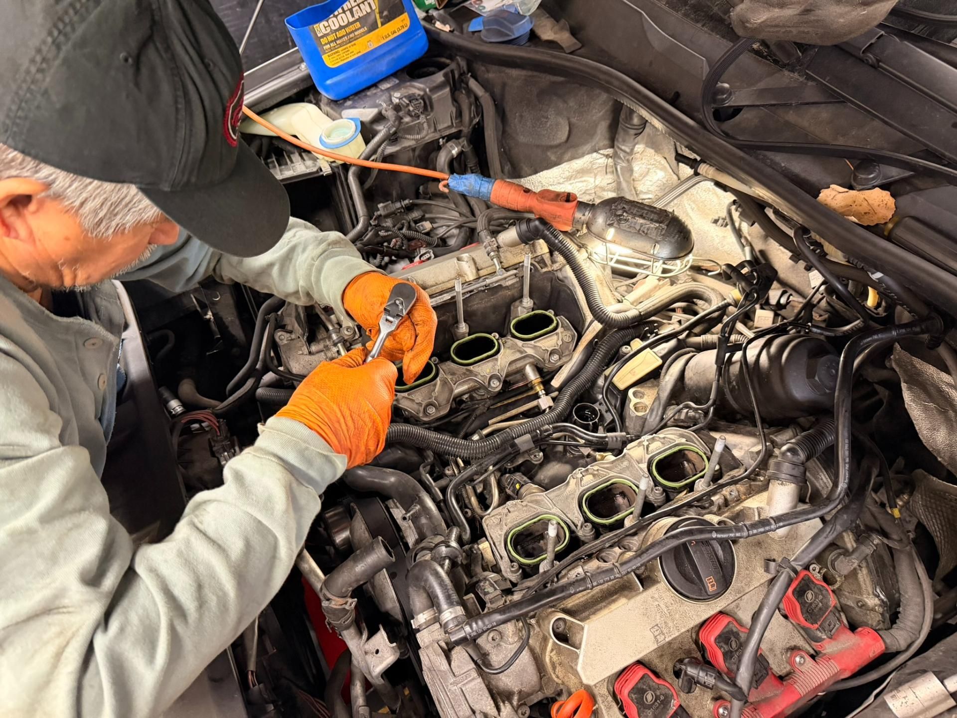 Mechanic inspecting an engine bay with a tool, surrounded by exposed engine parts and hoses.