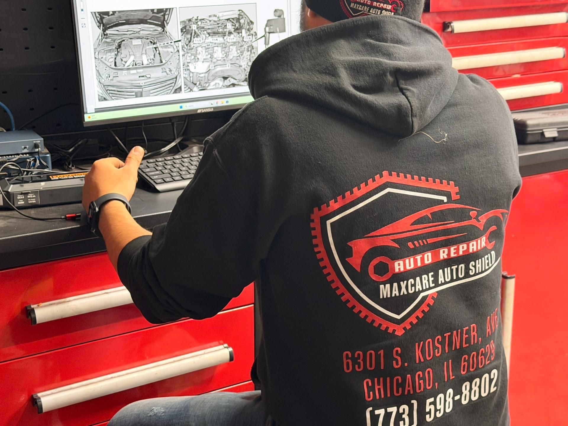 Person in black hoodie working on a red workbench with tools and a car repair monitor in the background