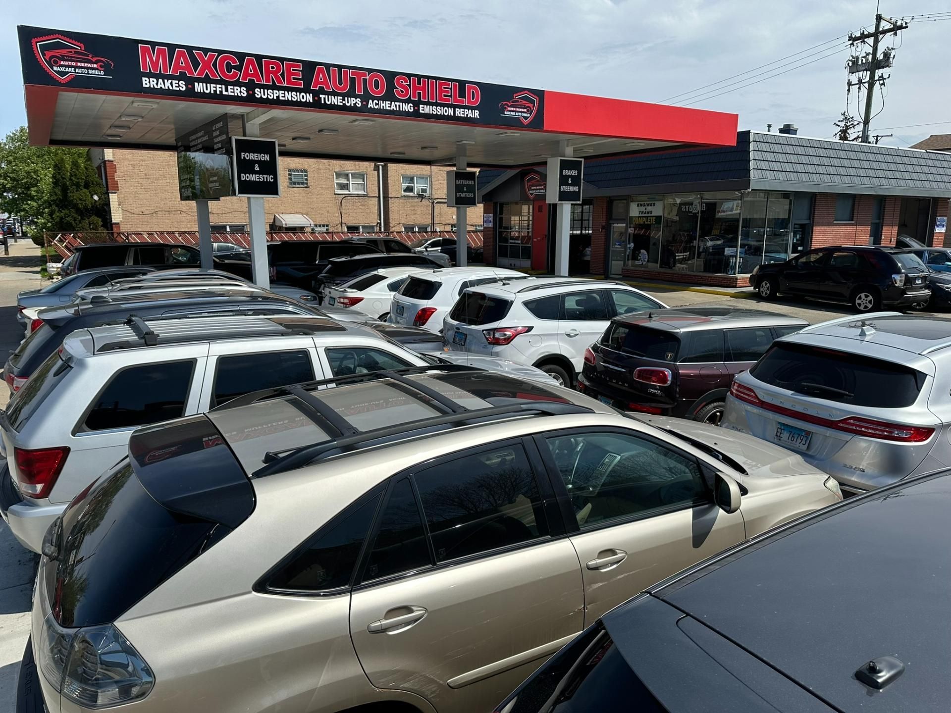 Car dealership lot with many parked cars under a red-and-black sign on a sunny day