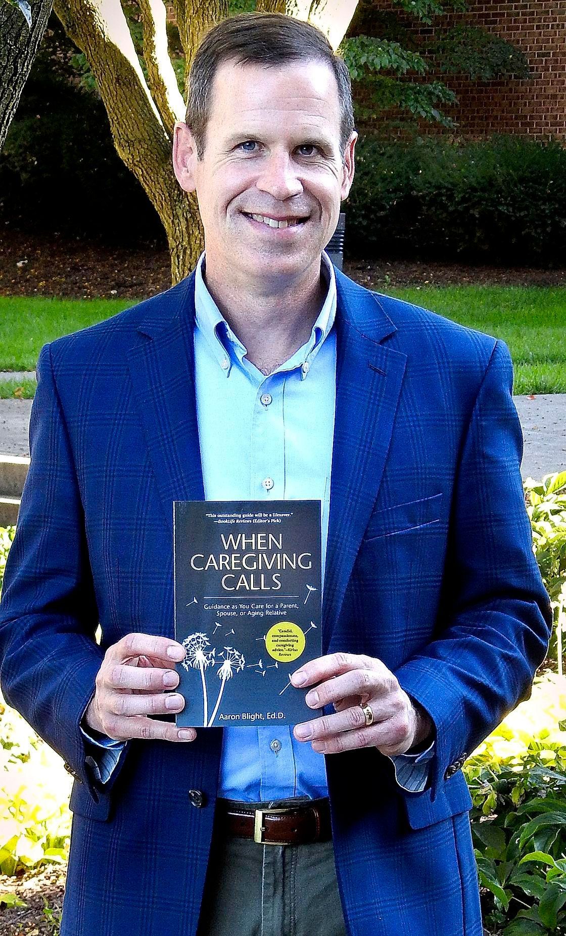Man in blue blazer holding a book titled