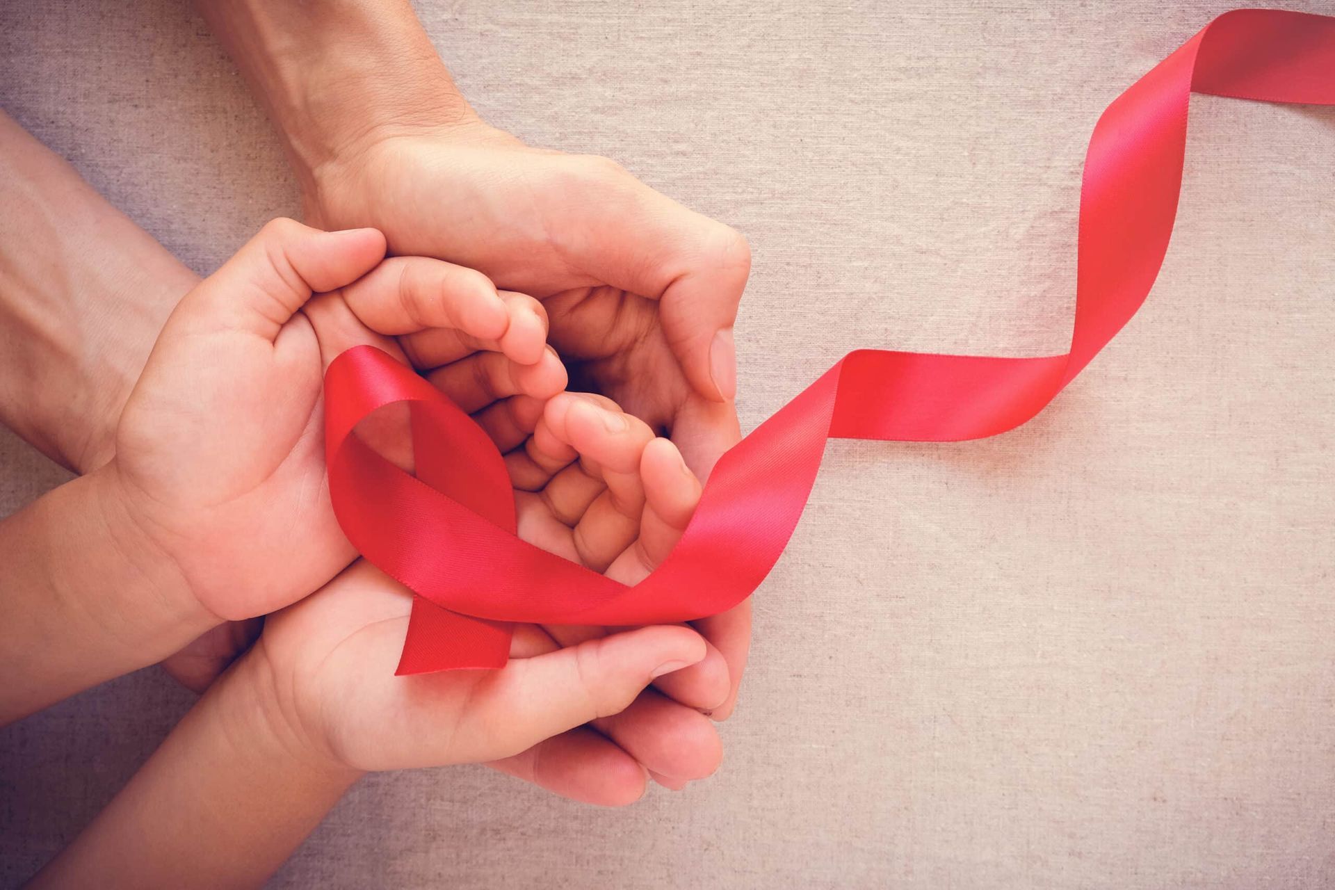 Two hands, one larger than the other, holding a red ribbon, symbolizing AIDS awareness.
