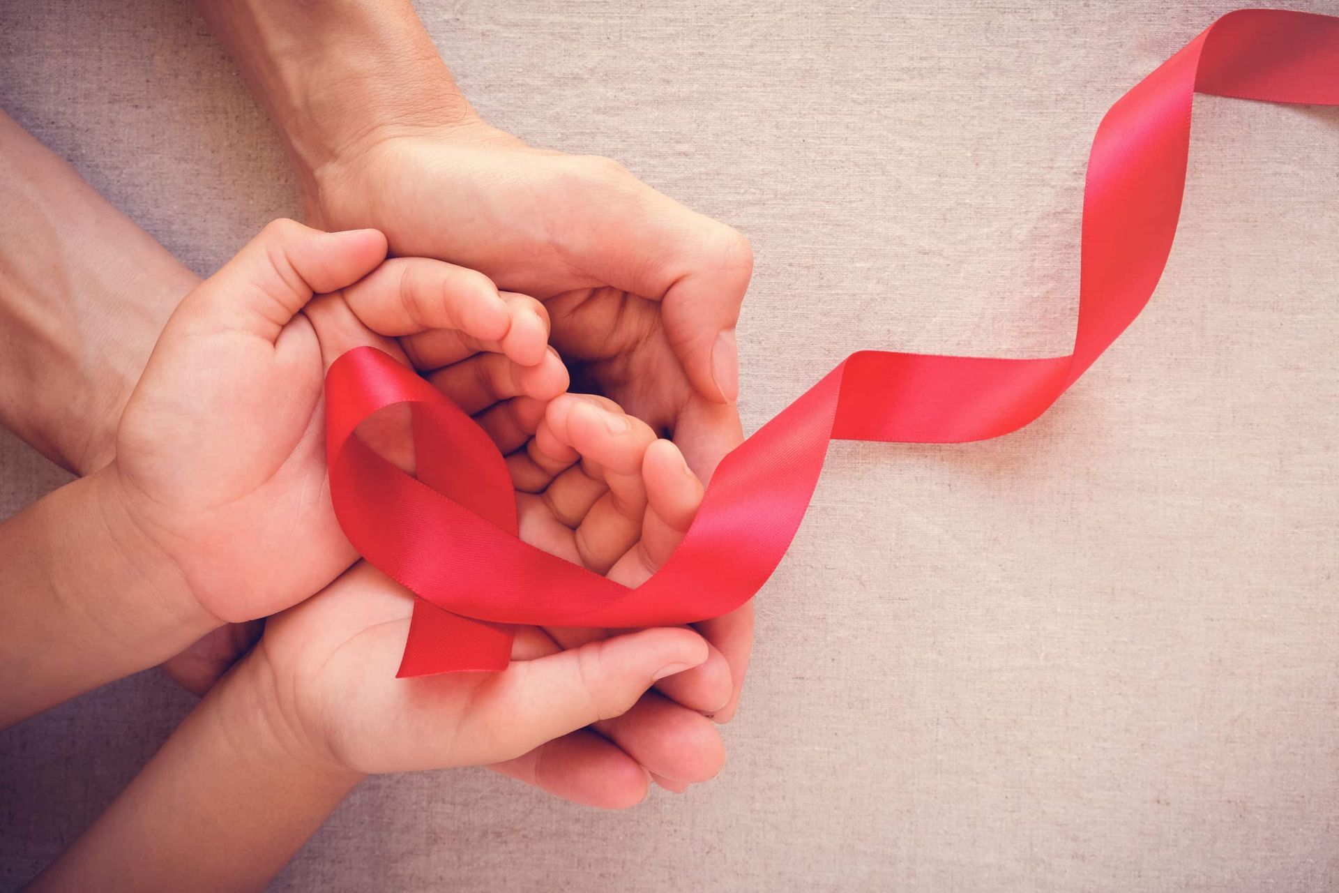 Hands holding a red ribbon, symbolizing AIDS awareness.