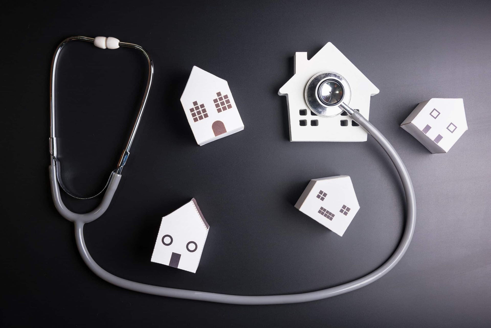 Stethoscope on tiny houses, metaphor for home health inspection. Dark background.