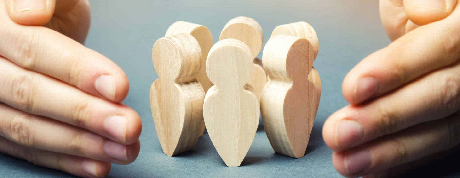 Hands cupping wooden figures of people, symbolizing protection and care.